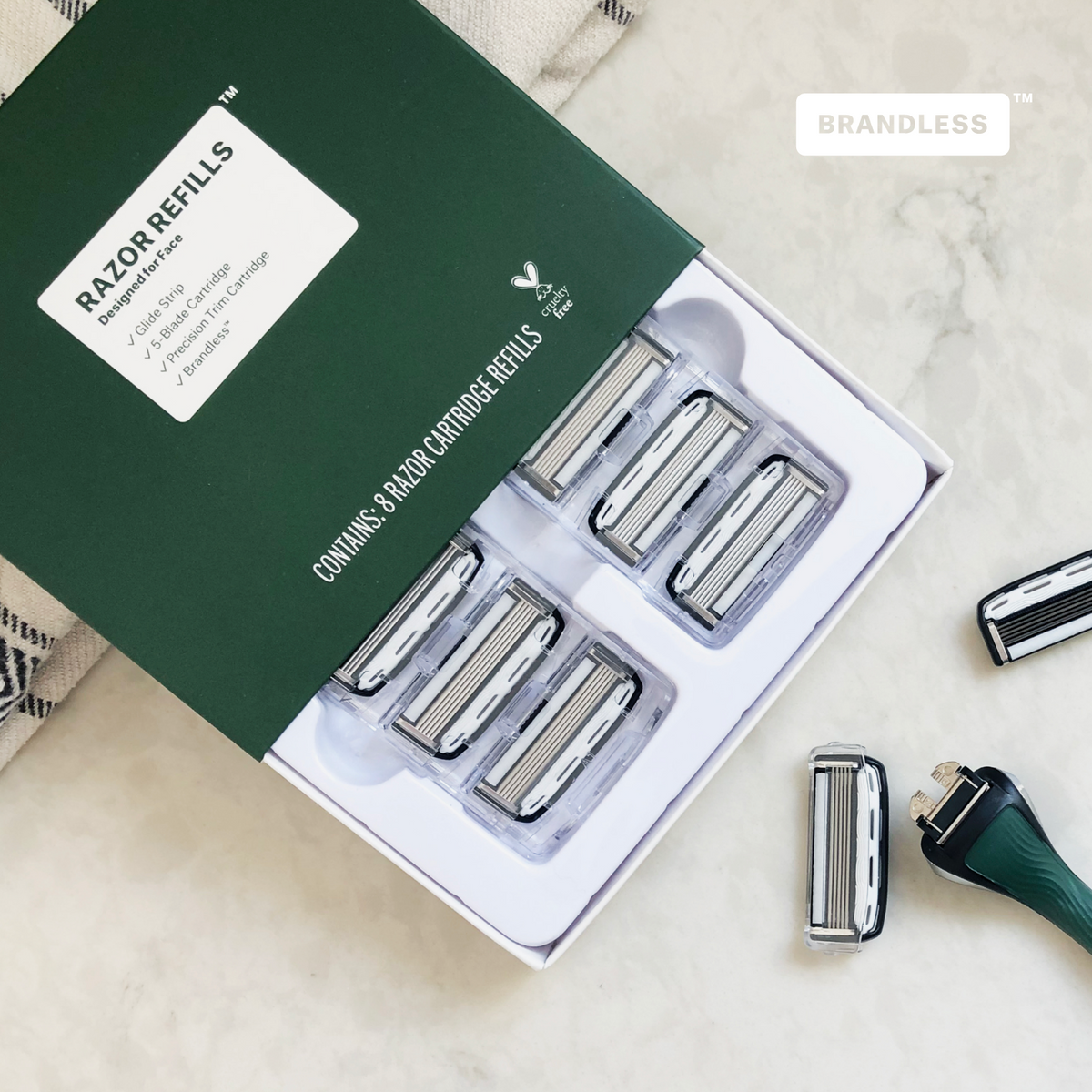 Lifestyle photo, razor refills for face, box slightly open and showing the razor refill cartridges, box sits on a white marble bathroom countertop next to a disassembled razor handle and cartridge pair.