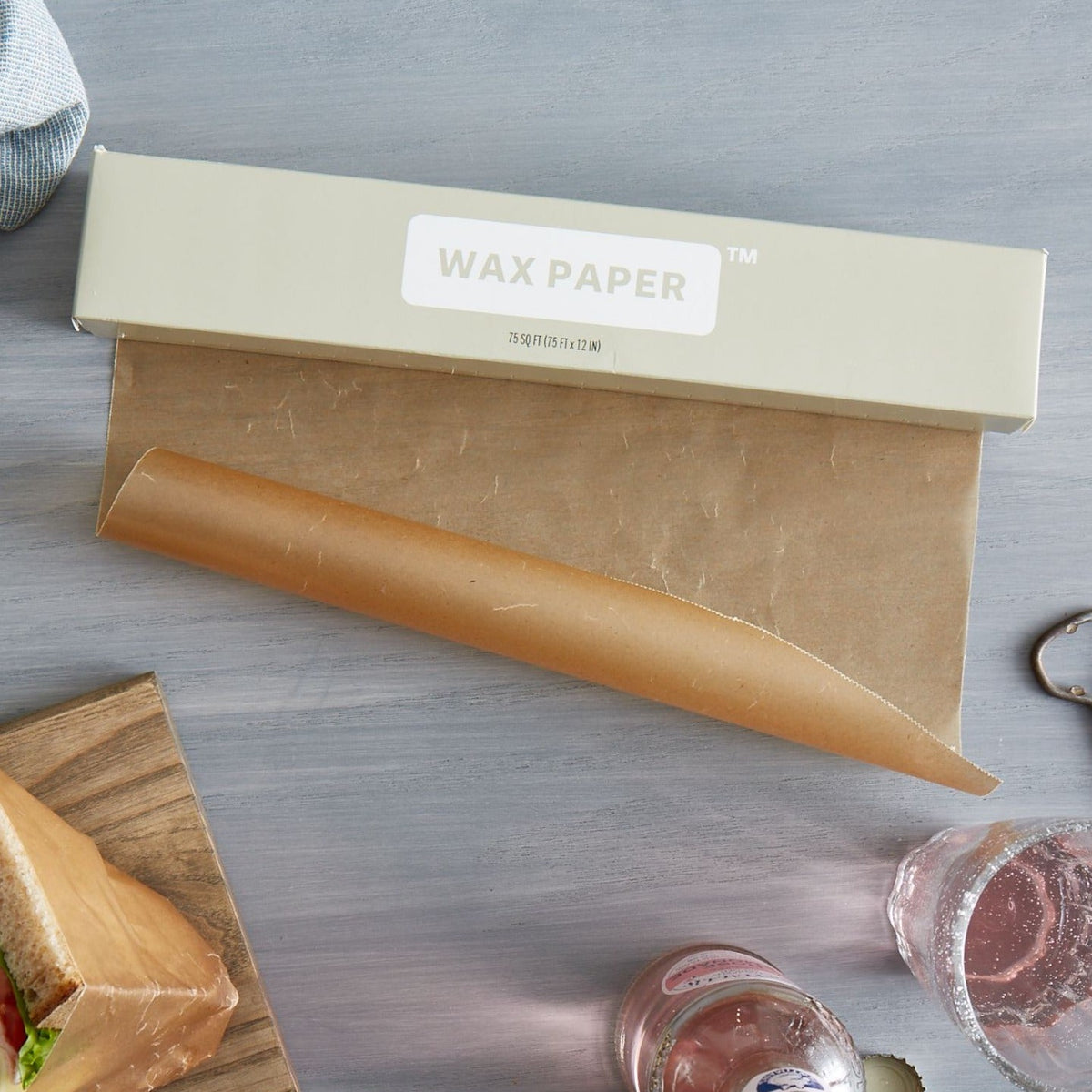 Lifestlye photo of wax paper being unrolled on a kitchen counter next to sandwiches.