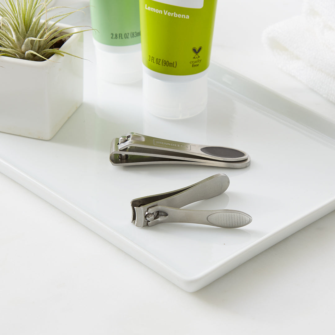 Lifestyle photo. Nail clipper set sits in a bathroom organizer tray next to a little succulent in a tiny white square pot and lemon verbena hand cream.