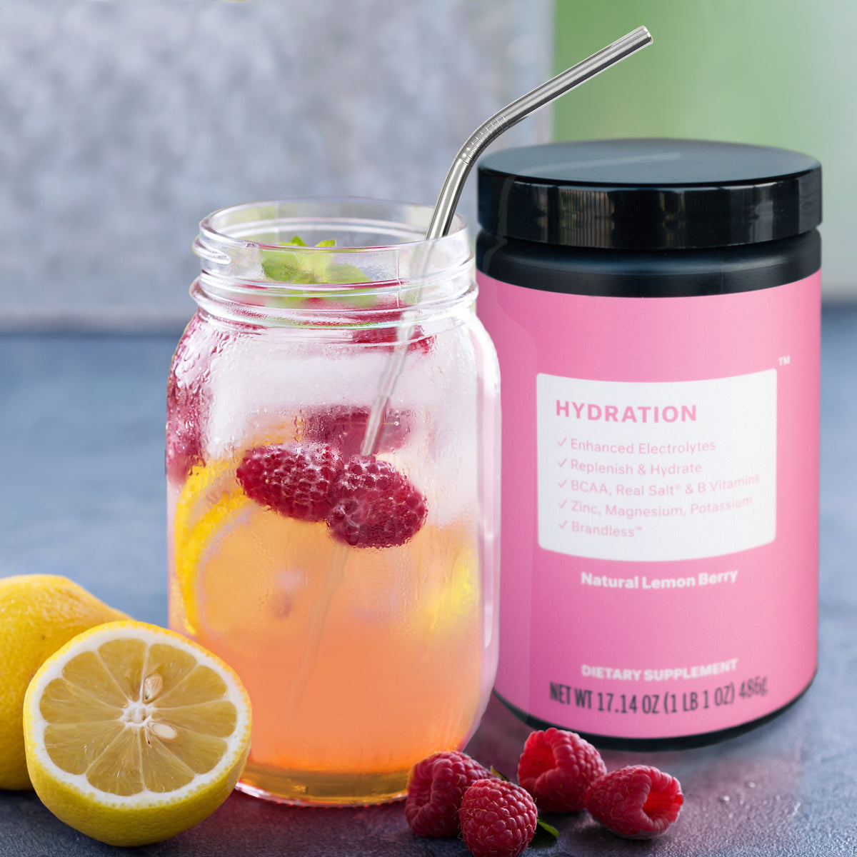 Lifestlye photo, Tub of Brandless Hydration powder next to a mason jar with fresh lemon slices and raspberries mixed into a beverage with the Hydration powder as the base.