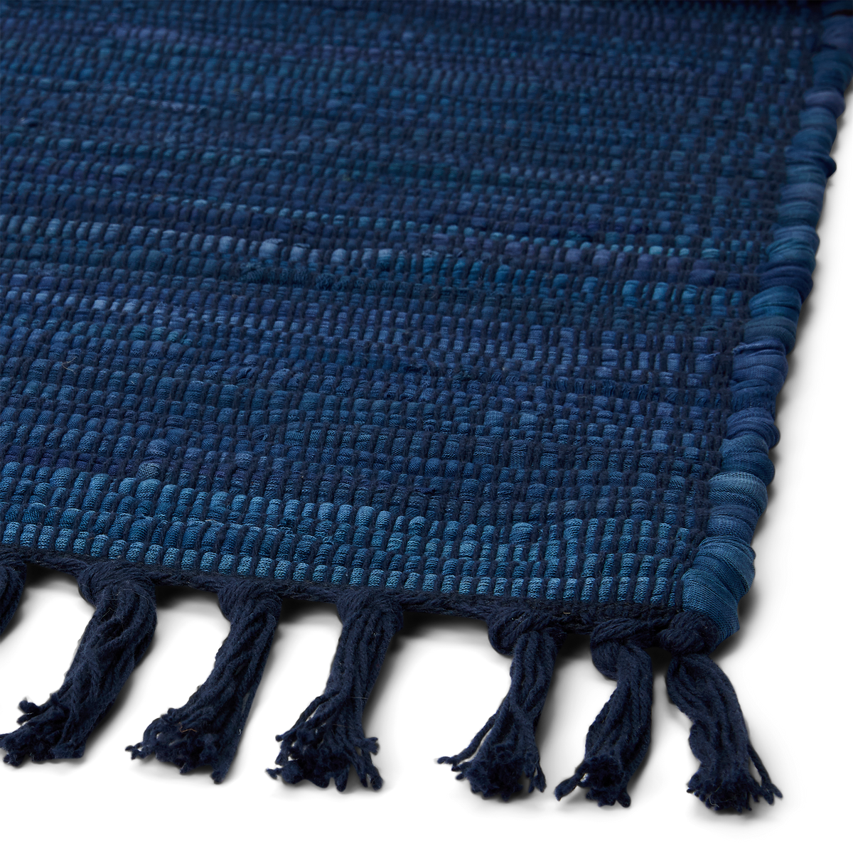 Detail view of blue recycled rag rug corner, showing fully sewn square corner and fringed ends.