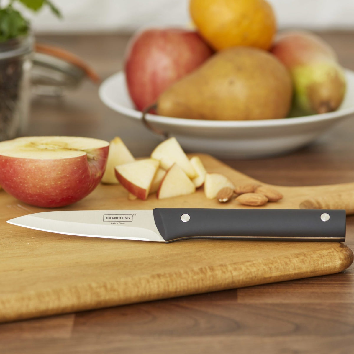 Lifestyle photo, paring knife laying on a wood cutting board on a kitchen table with a diced apple, some almonds, and pears ready to be sliced.