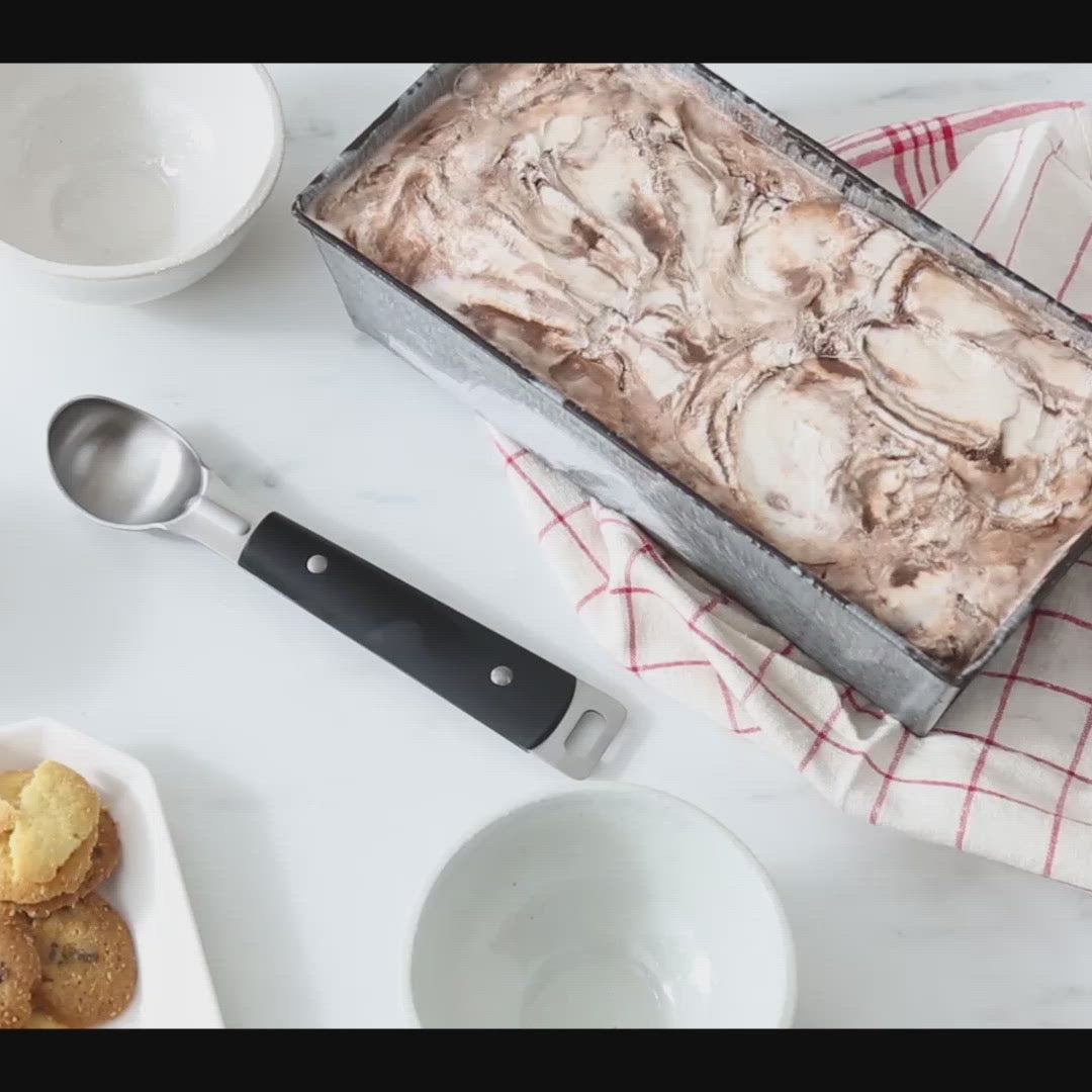 Video, no sound. Woman scoops up delicious-looking swirled chocolate and vanilla ice cream from a pan into a bowl with the Brandless Ice Cream Scoop