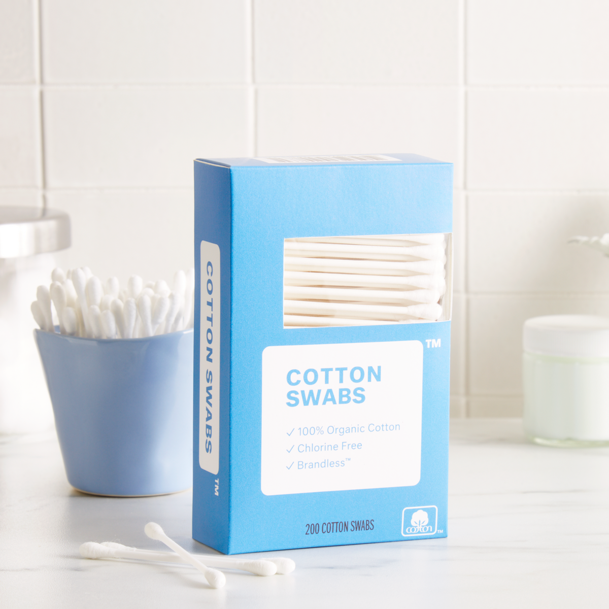 Lifestyle photo. Box of cotton swabs sits on counter next to a small ceramic cup full of swabs on a bathroom counter.Cotton Swabs. 100% organic cotton. double tipped. chlorine bleach free. hypoallergenic. Brandless.