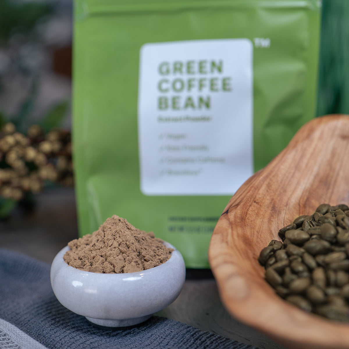 Green coffee bean extract powder in a small marble bowl in front of the product bag, with whole green coffee beans in a wood container to the side.