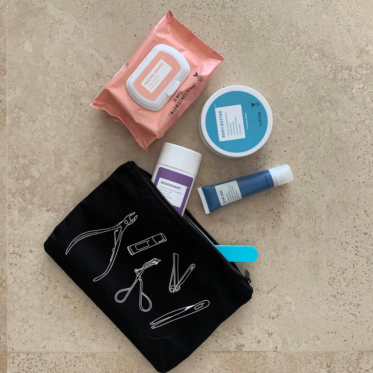 Lifestyle photo, showing the cosmetic bag with several items poking out of it on a bathroom countertop, including makeup removal wipes, body butter, eye gel, deodorant, and an emory board.