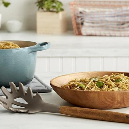 Lifestyle photo, silicone pasta fork laying nexxt to a pot full of pesto noodles, having just served a bowl full of the noodles.