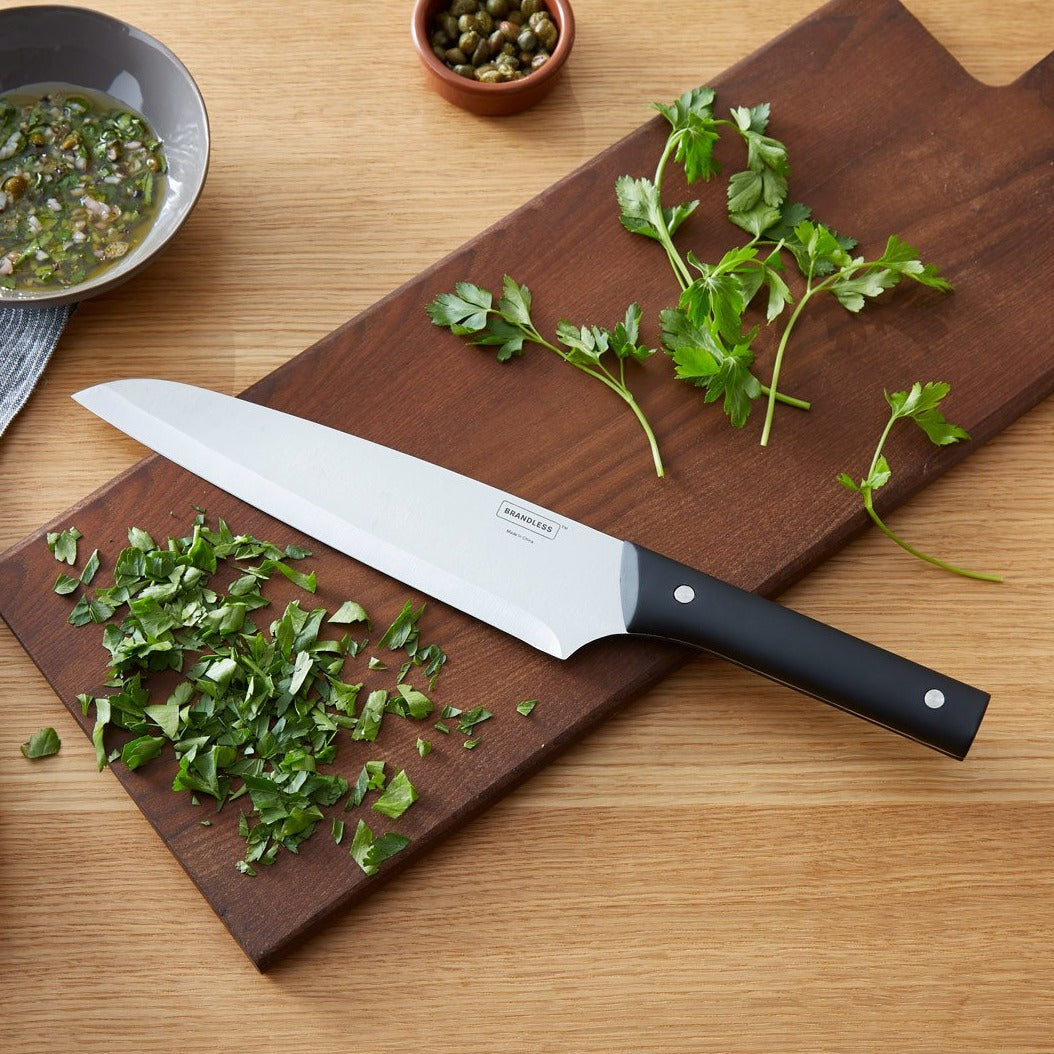 Lifestyle photo, 8 inch chef's knife laying on a cutting board with minced parsley.