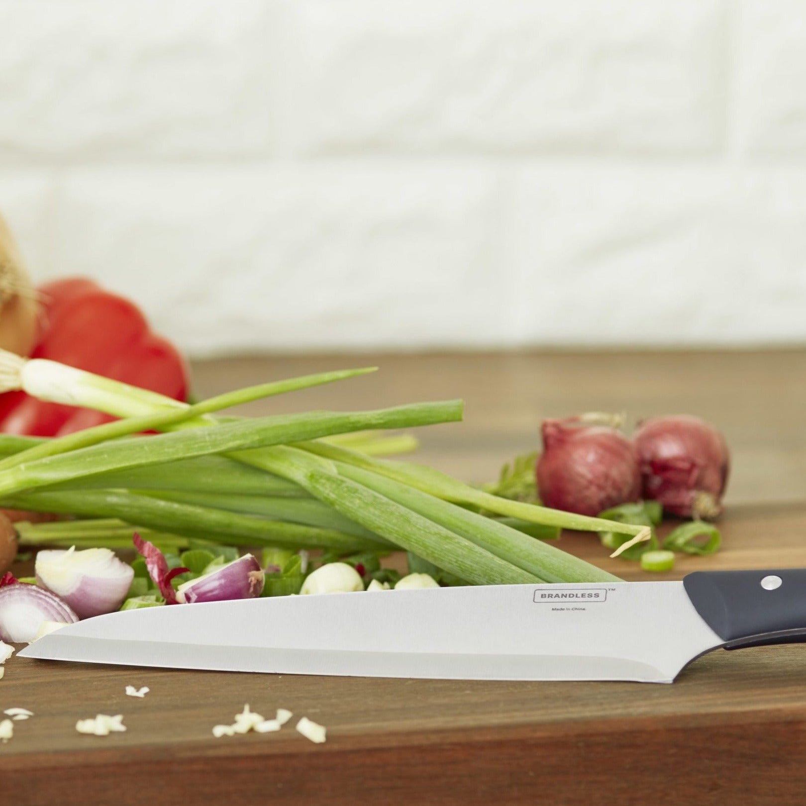 Lifestyle photo of the 8 inch chef's knife leaning on a cutting board with onions, shallots, and peppers on it.