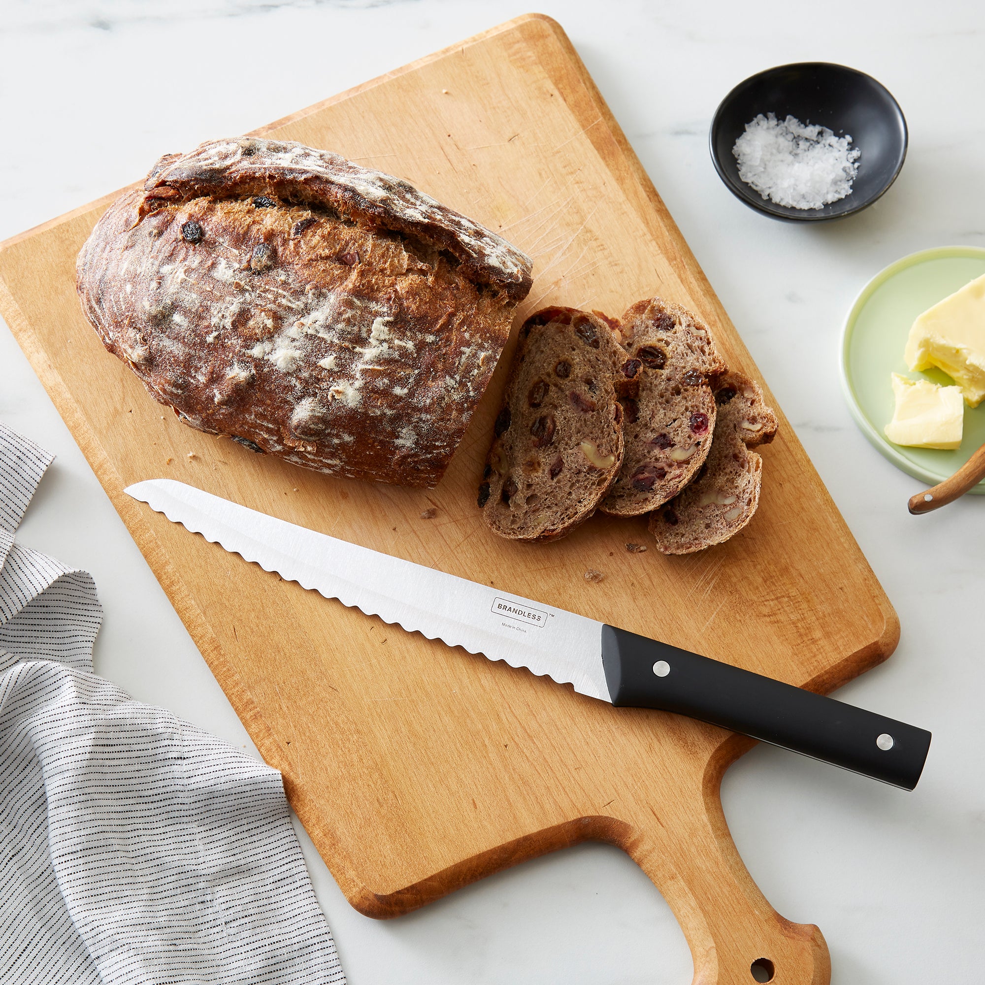 Brandless 8 inch bread knife laying on a cutting board next to a loaf of sliced bread.