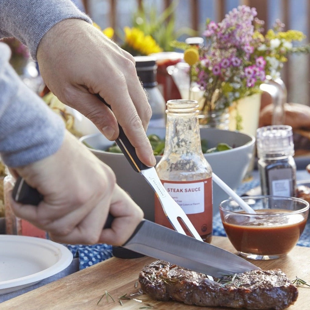 Lifestyle photo, man's hands holding carving knife and carving fork and slicing into a steak on a cutting board.