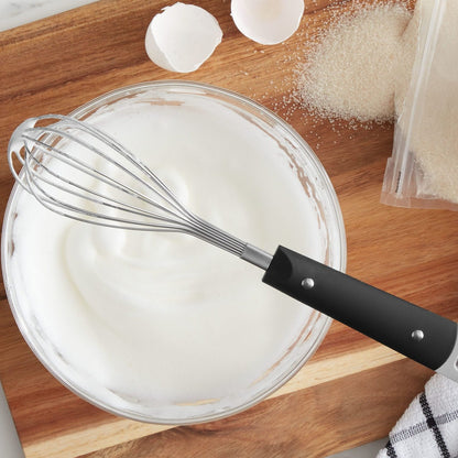 Top view, brandless wire whisk sits atop a glass mixing bowl with a fresh merange whipped up by the whisk and ready to top a fresh pie.