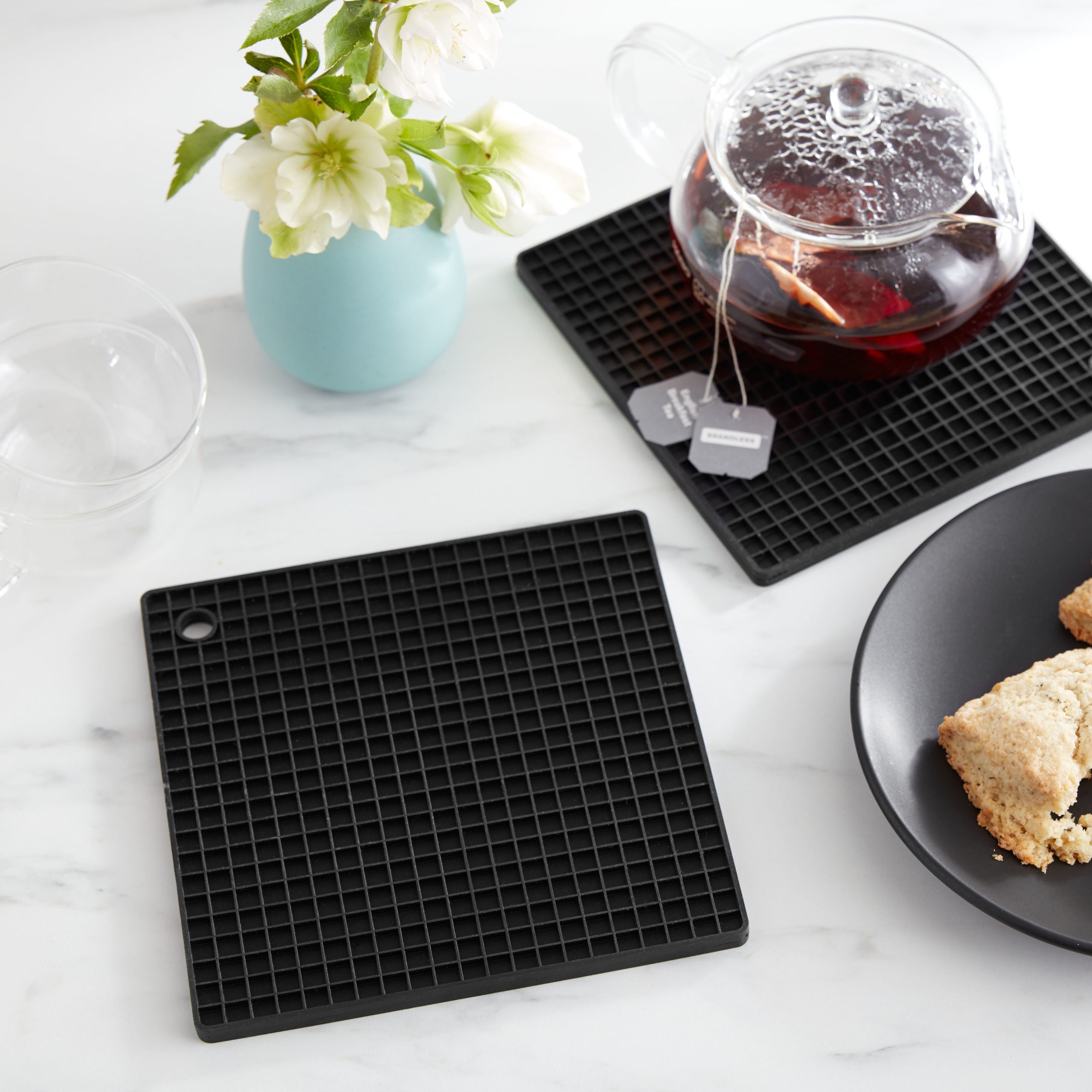 Lifestyle. Kitchen counter scene with black silivone trivet on marble countertop protected by silivong trivet with hot tea pot.