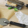 Video, no sound.  Woman uses Brandless pizza cutter to effortlessly slice a homemade margherita pizza with fresh tomatos and basil leaves.