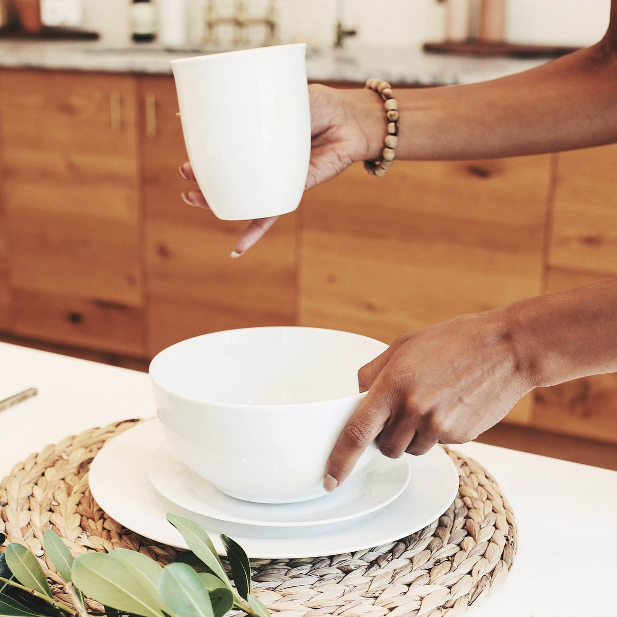 Lifestyle, woman places a white porcelain coffee mug onto a beautifully decorated dining room table complete with stacked white porcelain bowl and plates.