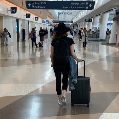 Lifewstyle photo of a woman walking through an airport with a brandless wheeled luggage bag.