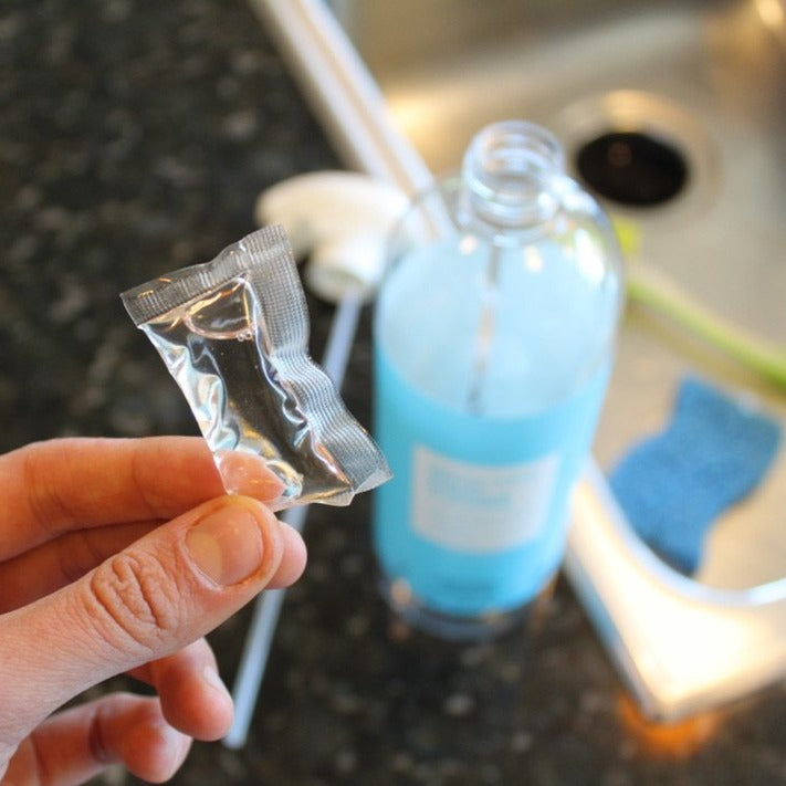 Lifestyle photo, woman inserts a cleaning pack into an empty refillable multi surface cleaner bottle.  Once inserted, she'll add 32oz of tap water to create a whole new bottle full of multi surface cleaner.