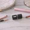 Video, no sound.  Woman demonstrates sharpening a large beauty pencil using the large opening on the left of the dual sharpener, then flipping it over and sharpening a regular sized beauty pencil with the other end, then flipping it back over on the counter without leaving a mess of shavings as the sharpener keeps shavings internally from both blades.